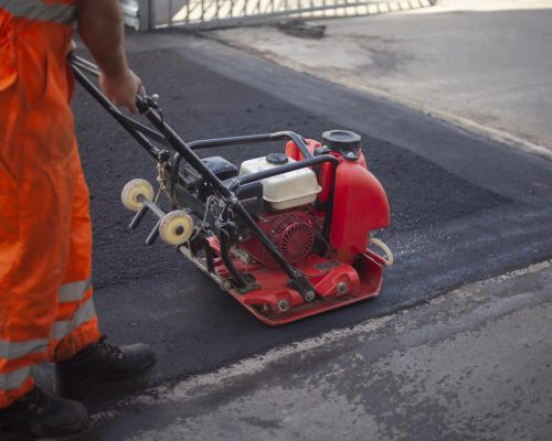 Asphalt laying. Leveling the road. A worker compresses warm asphalt. Road surface repair.