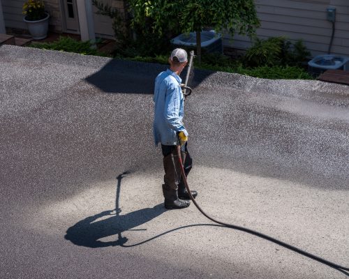 Workers applying blacktop sealer to asphalt street using a spray to provide a protective coat against the elements